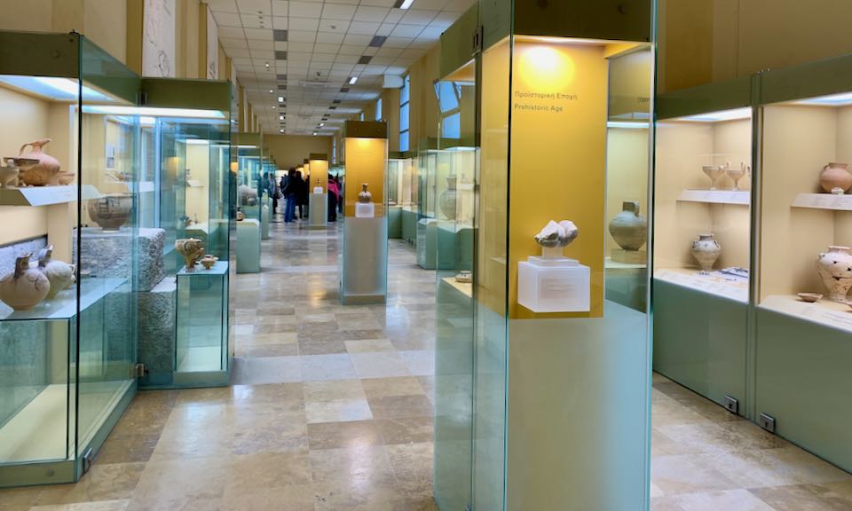 Museum corridor lined with lit display cases, filled with ancient artifacts