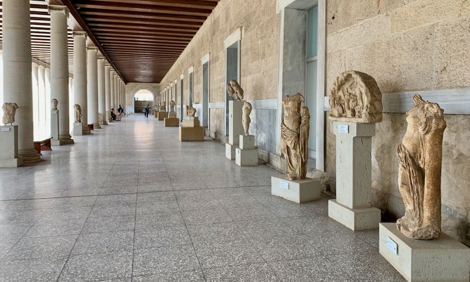 Marble statues on pedestals under a wood beamed colonnade