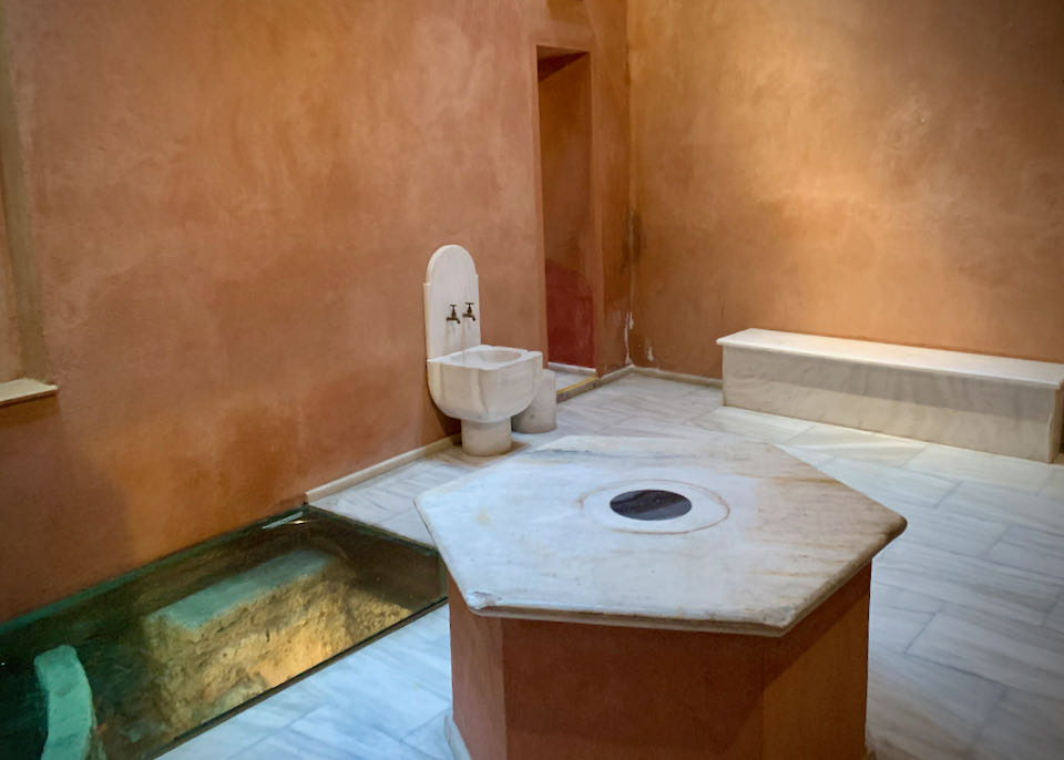 Room with terra cotta walls, marble floor and basins, and visible stone ruins below