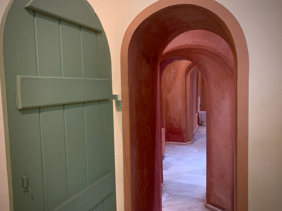Green wooden arched door leading to terra-cotta passageways