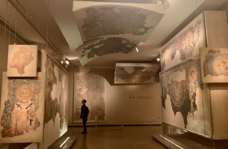 A museum goer looks up at a byzantine fresco in a museum gallery full of them