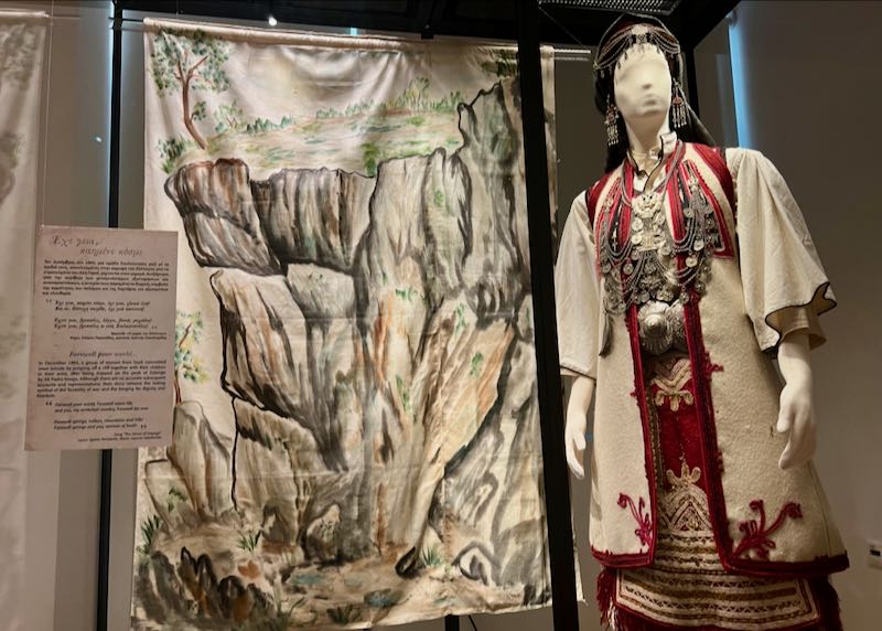 Mannequin in traditional Greek dress, displayed next to an artistically-decorated textile
