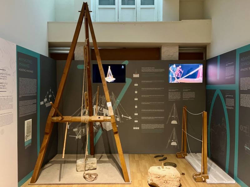 Wooden model of a pulley mounted to an easel-like structure, in a museum gallery