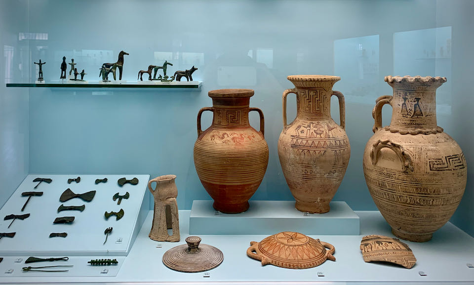 Clay vases and metal figures on display in a museum