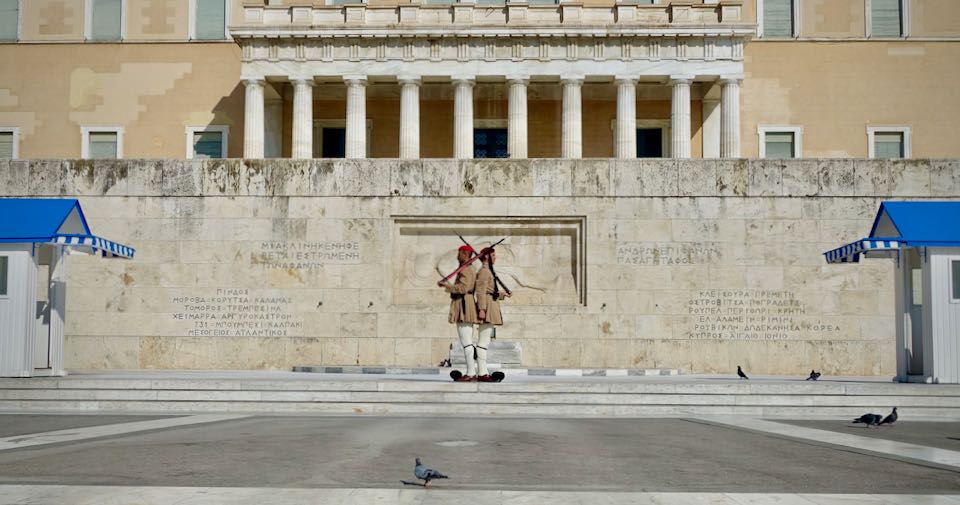 Two Greek military guards stand back-to-back in front of the Tomb of the Unknown Soldier