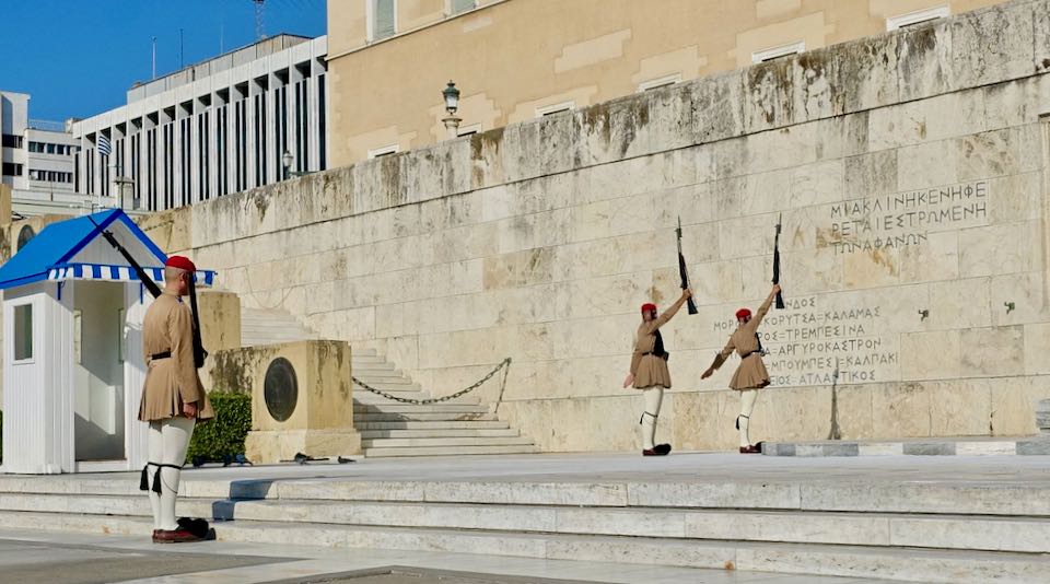 Two members of the Greek military guard stand with rifles raised in tandem