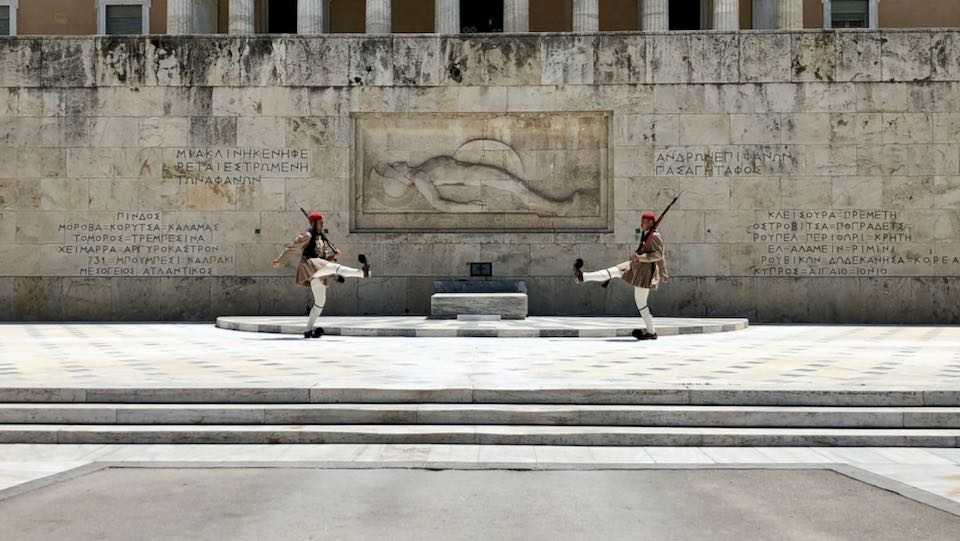 Two evzones face each other with legs raised on either side of the Tomb of the Unknown Soldier