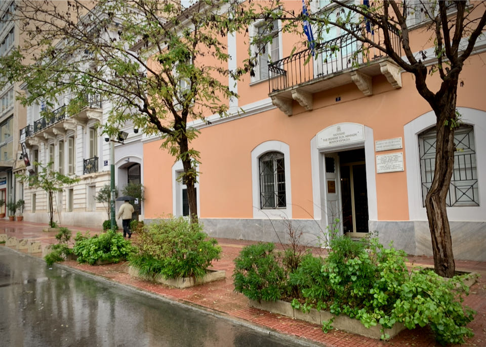 Exterior of a peach-colored neoclassical mansion on a city street on a rainy day