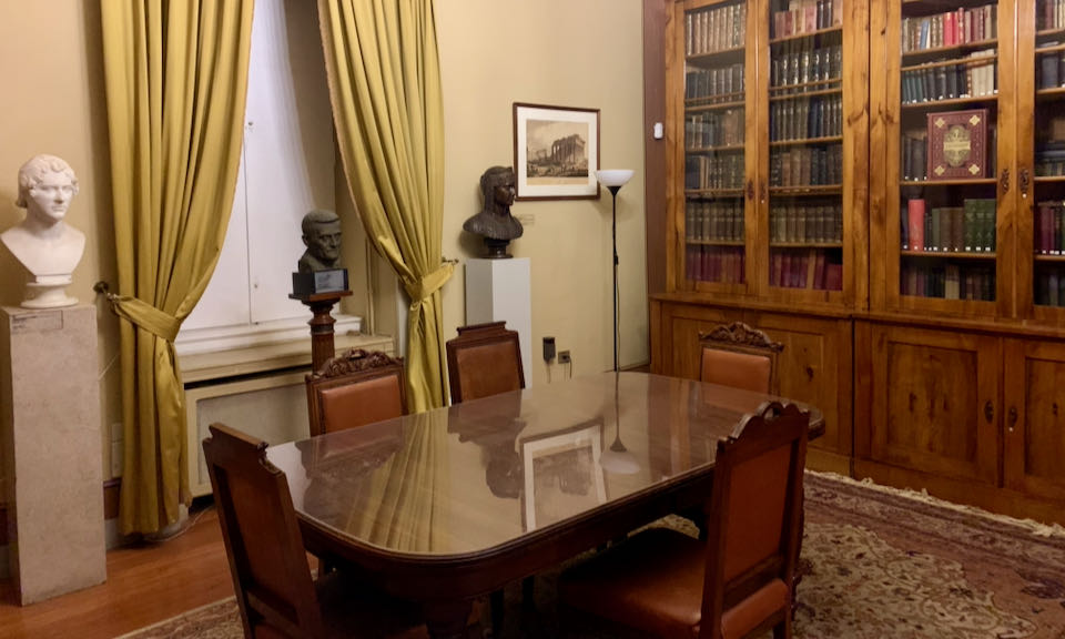 Library with built-in wooden bookcases, an elegant table, and statues on pedestals