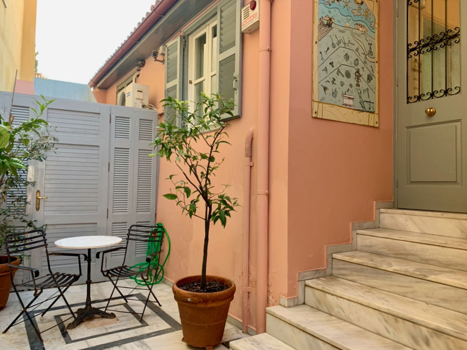 Small terrace outside of a pink building, with a cafe table and a potted tree