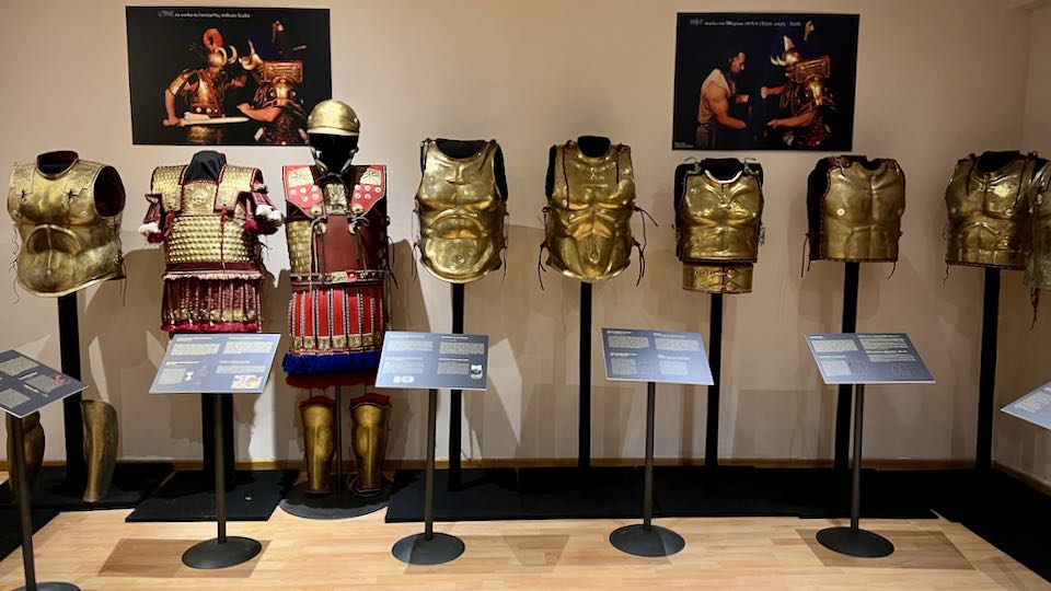 Brass breastplates lined up alongside one suit of armor
