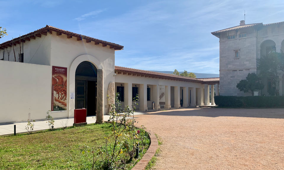 Two adjacent Mediterranean-style buildings in a red gravel courtyard