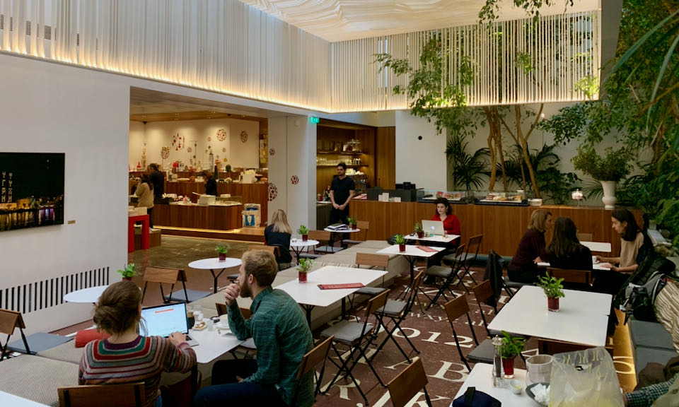 People sit and eat a cafe tables in a large, well-lit atrium