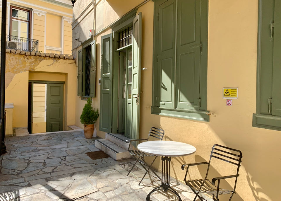 Cafe table and chair on a sunny terrace of a yellow building with green shutters