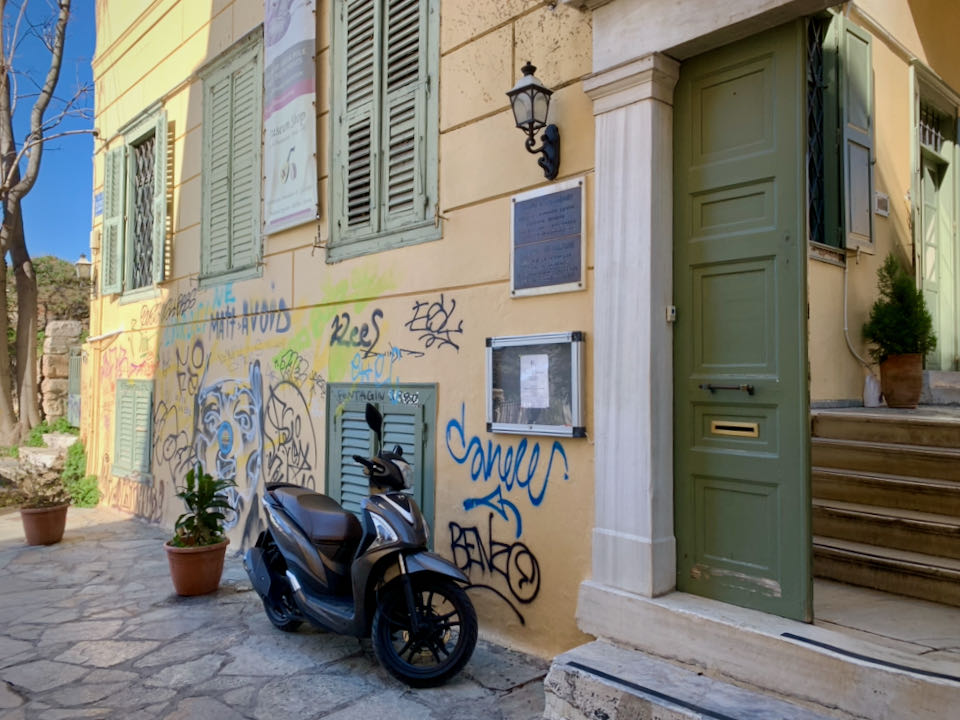 Open green doorway to a yellow grafitti-clad building with a motorcycle parked in front