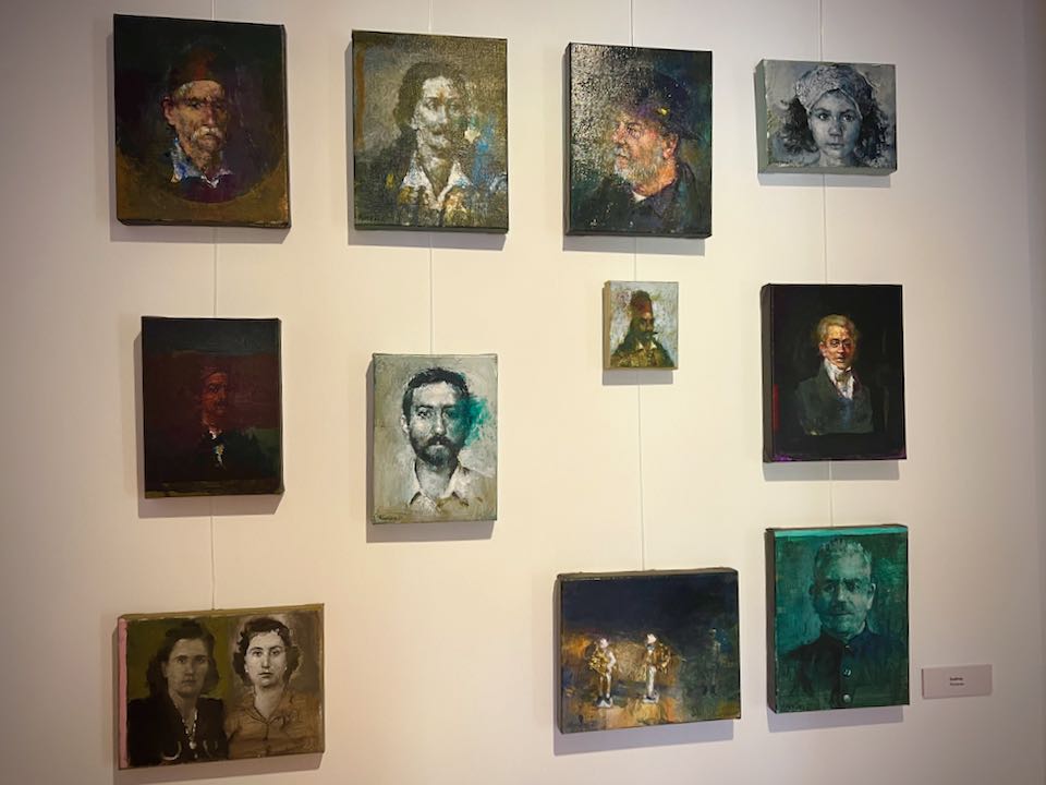 Small oil paintings depicting portraits of Greek historical figures, displayed on a gallery wall