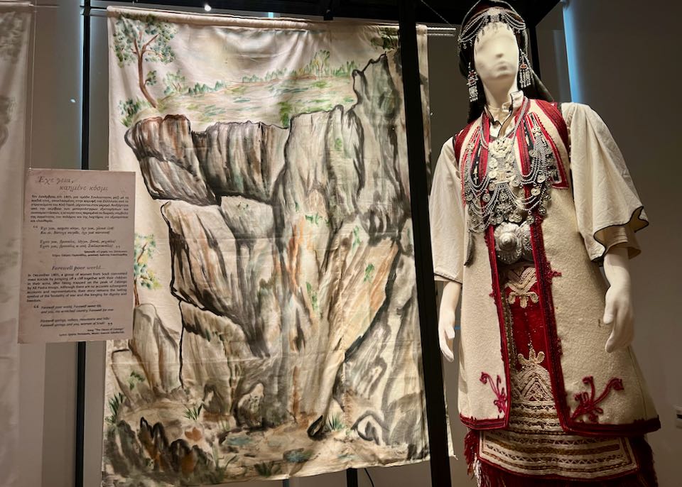 Mannequin dressed in traditional Greek costume, displayed alongside a decorative cloth