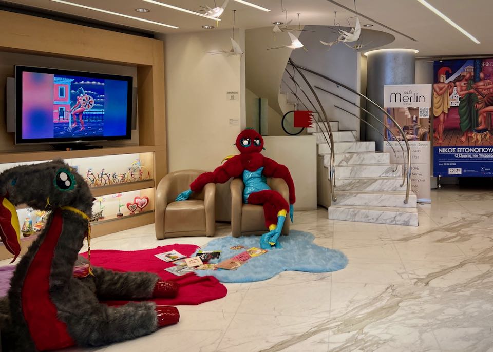 A large red, stuffed figure lounges on a chair in front of children's books