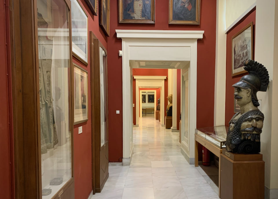 Red-pained hallway lined with paintings and statues