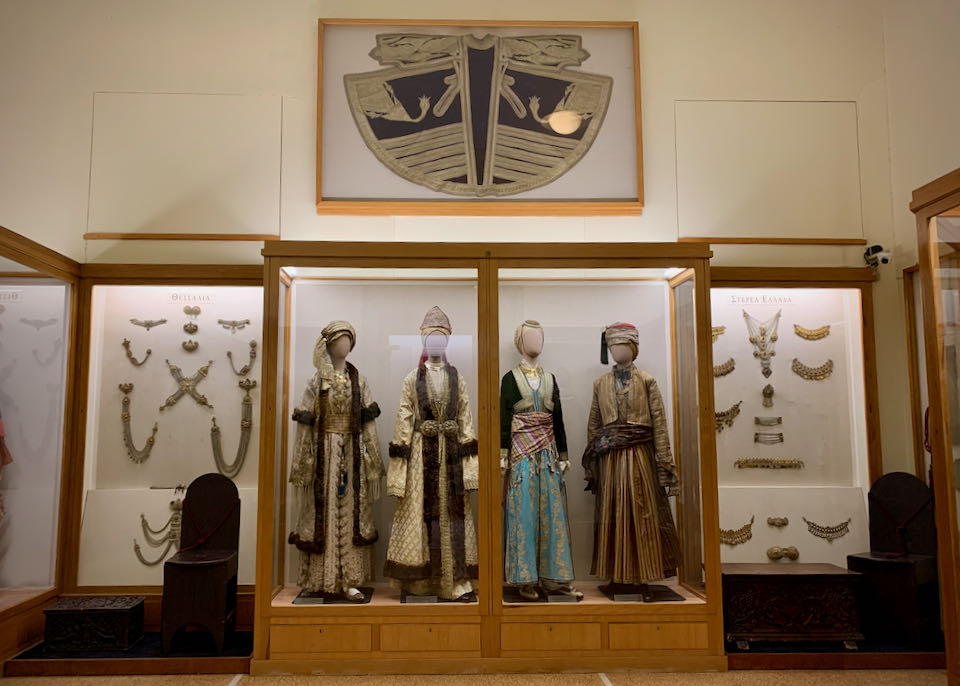 Traditional Greek clothing and jewelry on display behind glass