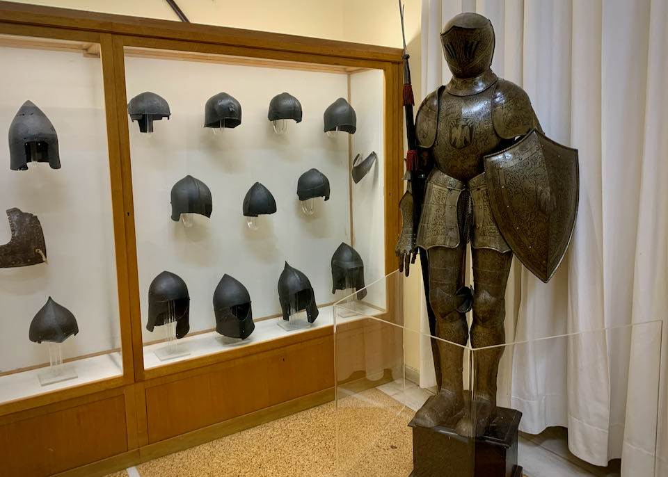 Suit of armor next to a museum display of helmets