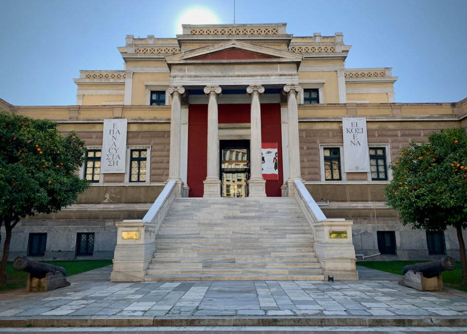 Cream and burgundy neoclassical building with marble steps leading up to a large pillared entryway