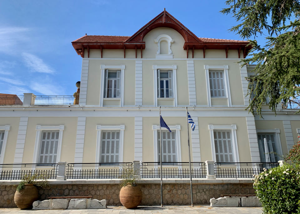 Yellow neoclassical-style building with Greek flag in front