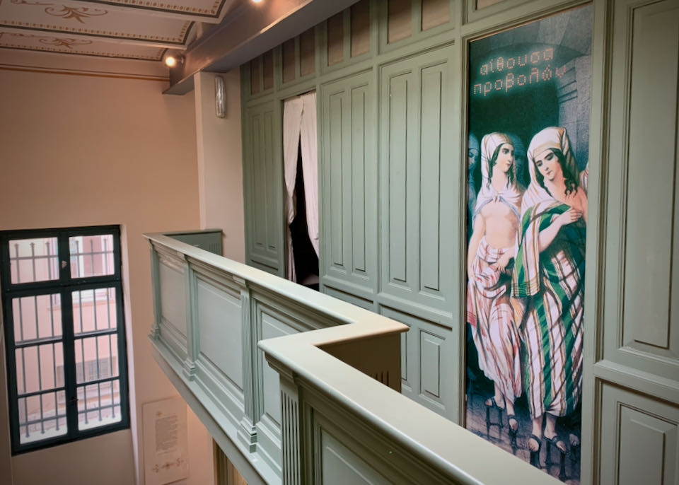 Sea green second-level corridor with curtained doorways and a painting of two Greek women