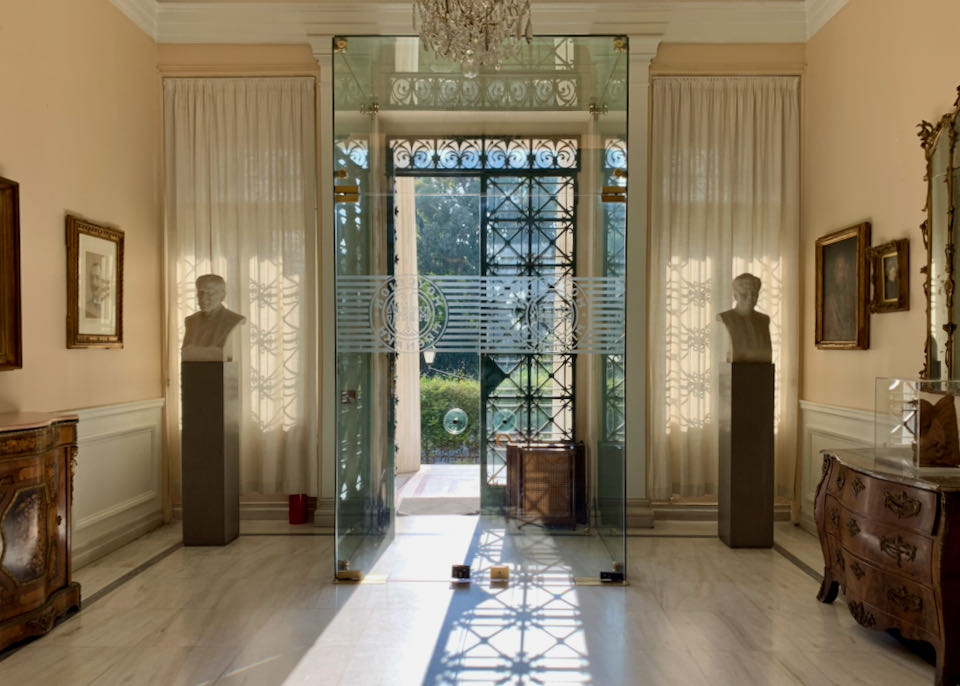 Sun streaming in onto a marble entryway through double entry doors with wrought-iron detail.
