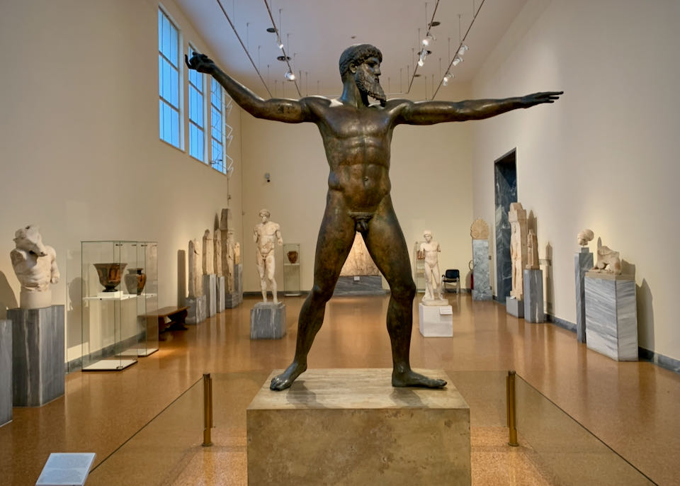 Bronze sculpture of a man throwing a spear in the middle of a room of other Greek sculpture