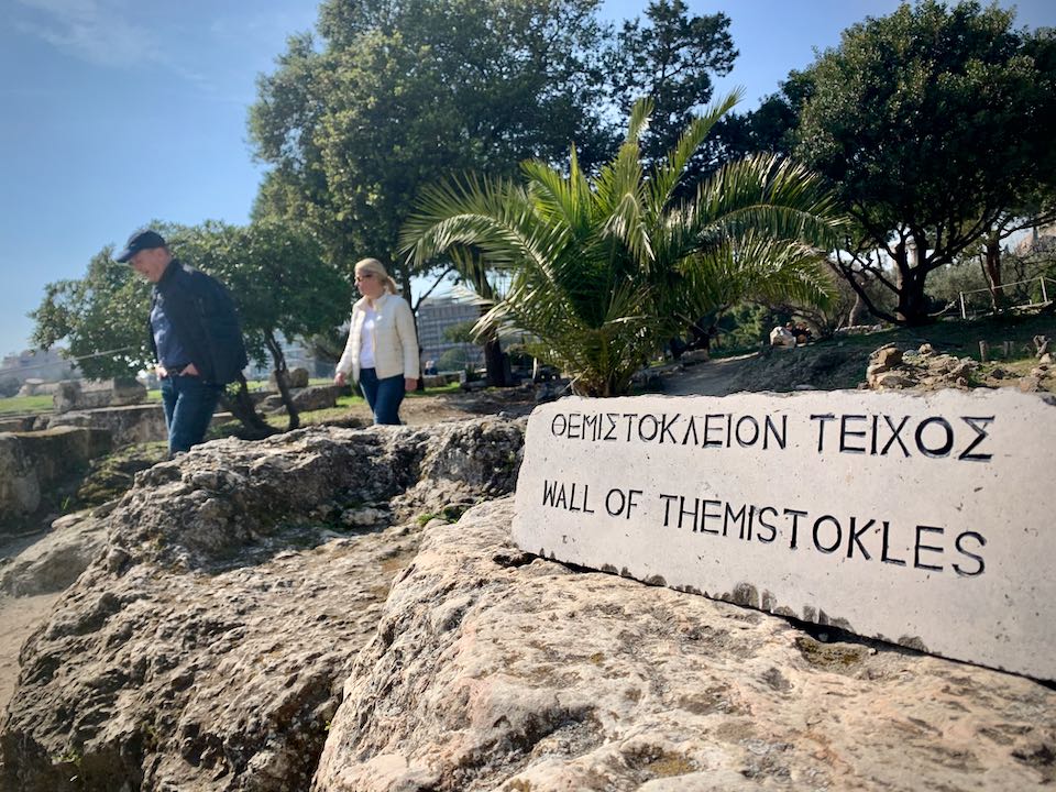 Sign sitting on a low stone wall, indicating that it is the Wall of Themistocles.