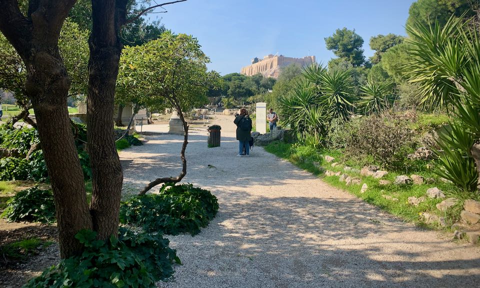 View along a tree-lined gravel path up to the Acropolis of Athens