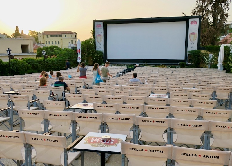 An outdoor movie screen at dusk, with patrons starting to sit down