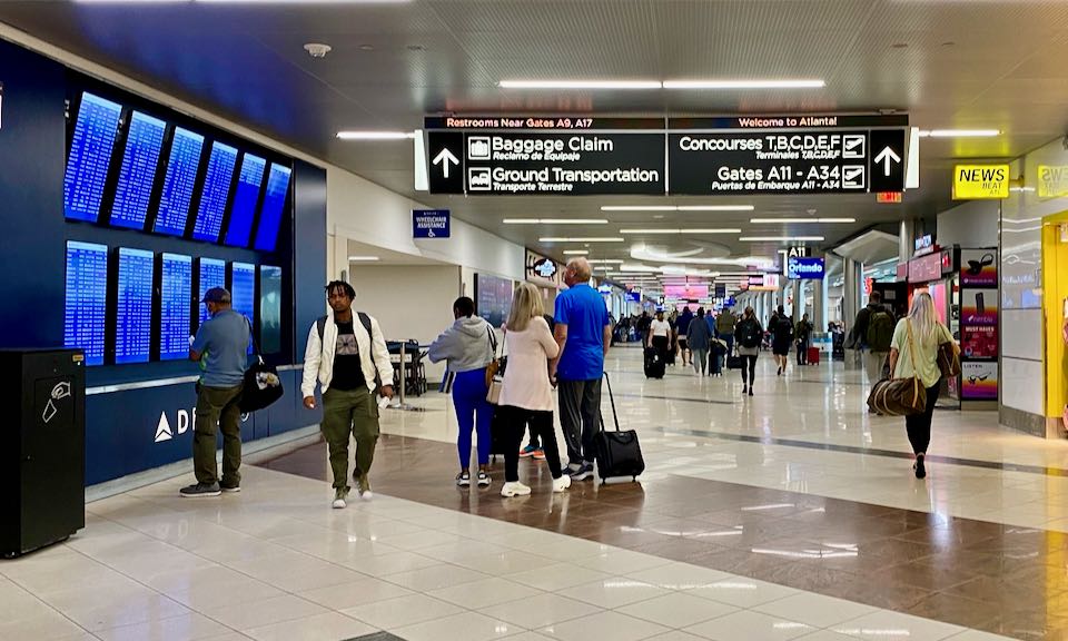 Travelers walk by display screens in a busy airport corridor
