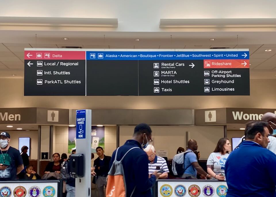 Inside the airport, a sign lists transportation options with a red "Rideshare" section with an arrow pointing to the right.