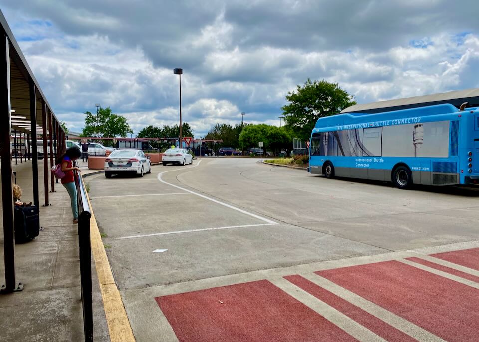 An outdoor waiting area with a railing and red crosswalk zone to a blue Connector bus.