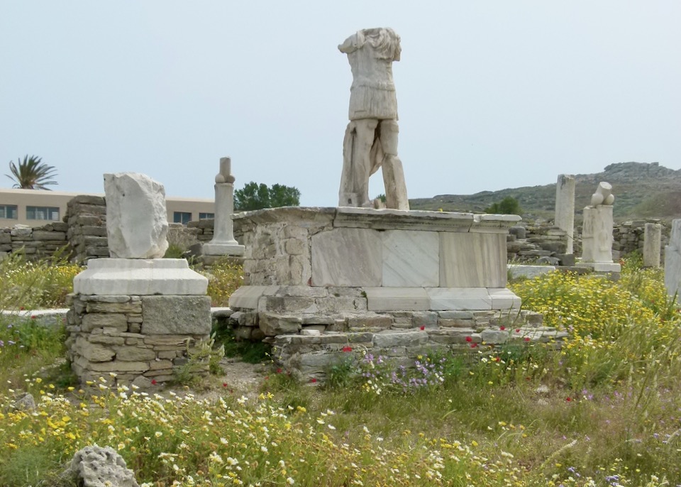 A ruined marble statue of a man, flanked by marble statues of male genitalia.