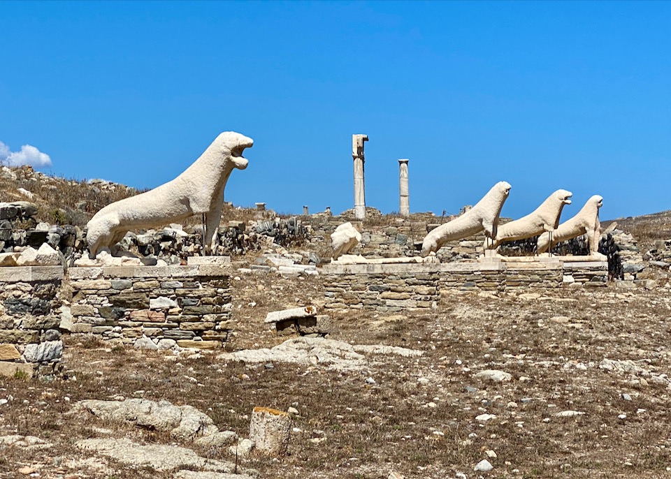 Weather-eroded stone lion statues sitting on rocky ground against a background of blue sky.