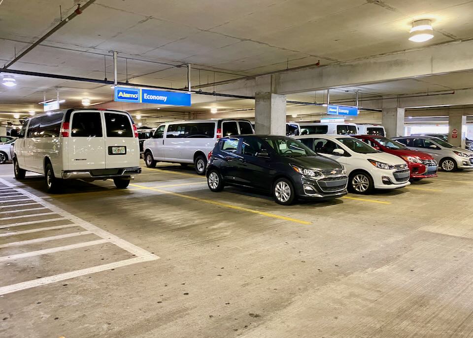 Several cars and a van sit parked in the Alamo section of the garage.