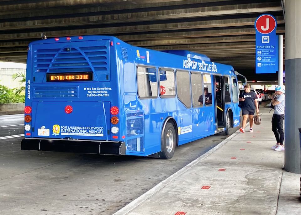 A blue bus pulls up to the curb.
