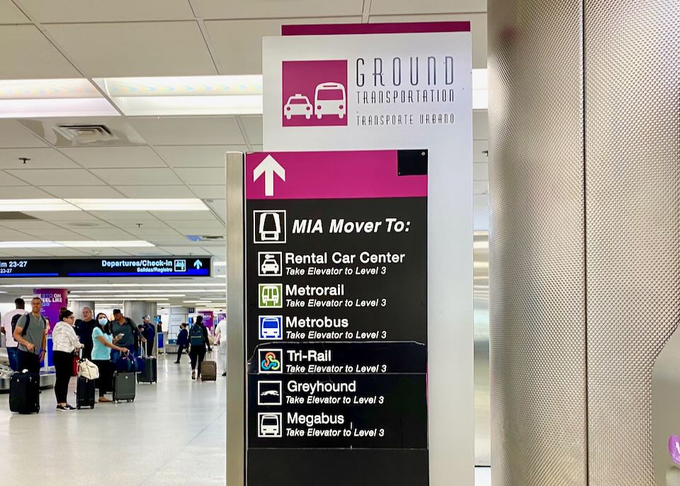 A pink sign with an arrow pointing up directs people to the MIA Mover and the rental car center.