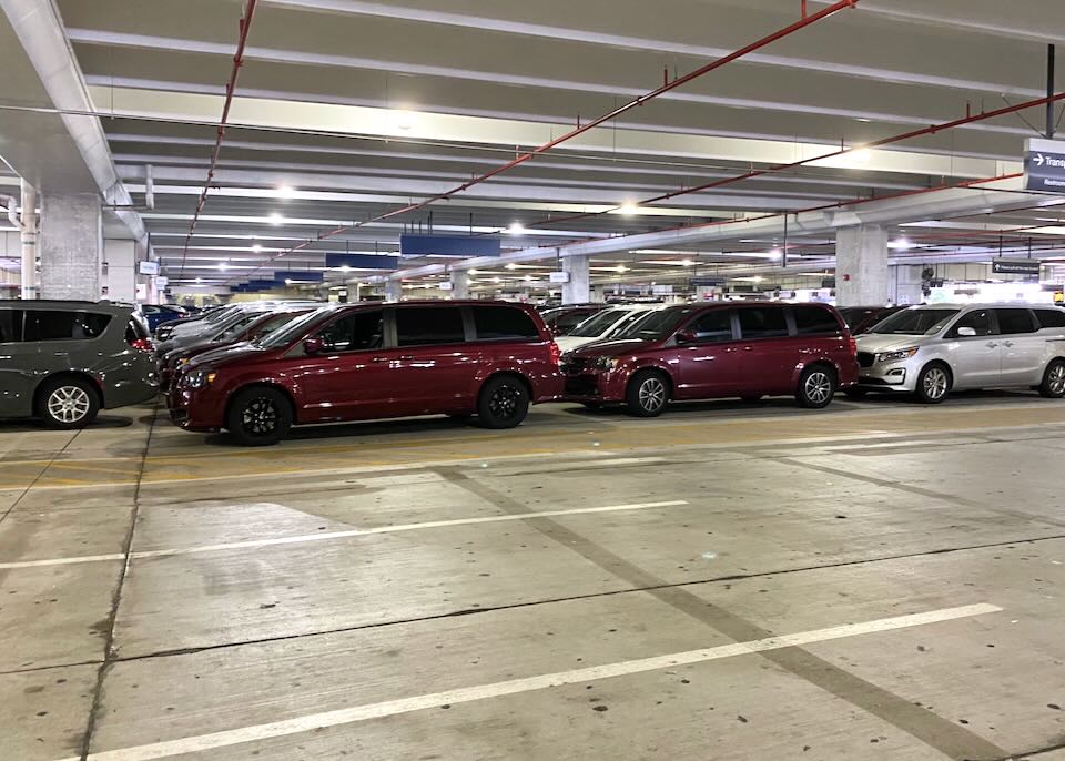 Burgundy minivans sit parked in the Avis lot.