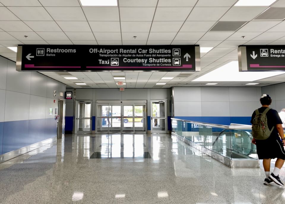 An overhead sign points to the Off-Airport Rental Car Shuttles outside the airport.