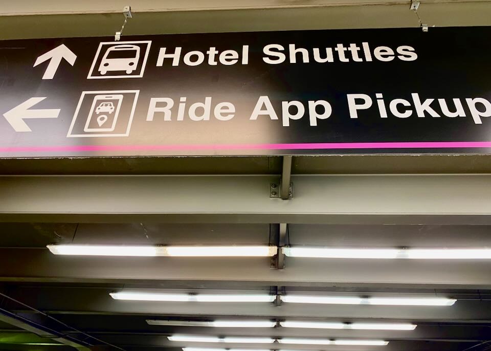 An overhead sign with arrows points left to the Ride App Pickup area.