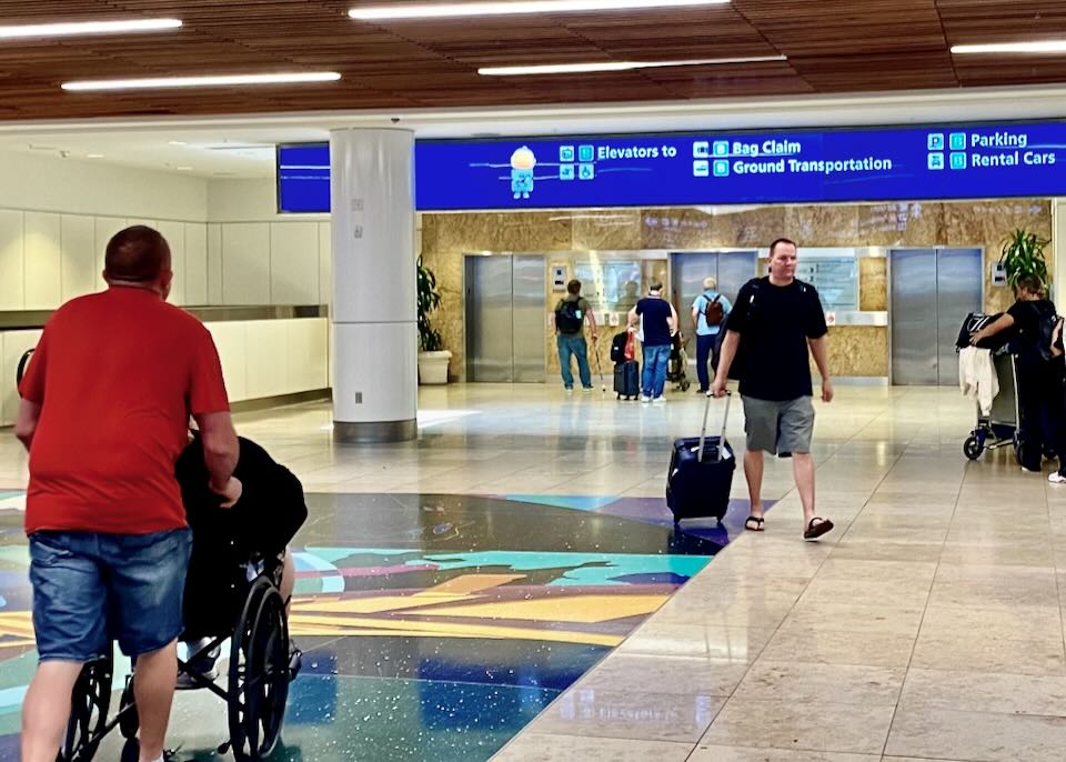 Passengers walk in front of the elevators that have signs to baggage claim, ground transportation, rental cars, and parking.