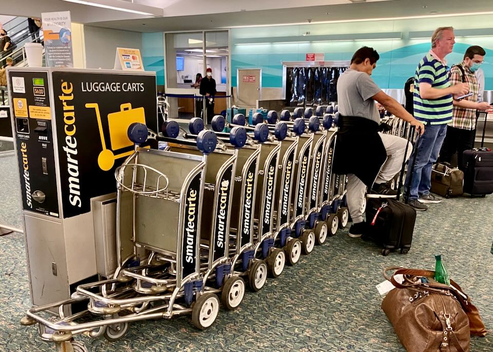 Passengers waiting for their luggage lean against the Luggage rental carts.