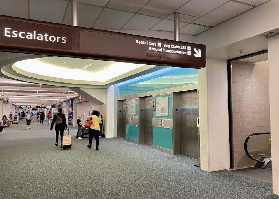 One overhead sign points down to an escalator that reads, "Rental Cars, Baggage claim 28B, and Ground Transportation."