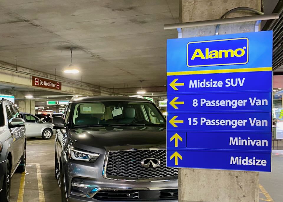 An Alamo sign points to Midsize SUVs, 8 Passenger Vans, 15 Passenger Vans, Minivans, and Midsize cars.