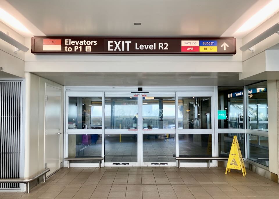 An overhead sign shows Exit level R2 to Payless, Budget, Avis, and Hertz rental car agencies.