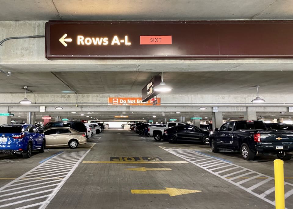 A sign above parked cars reads, Rows A-L Sixt, with an arrow pointing to the left.